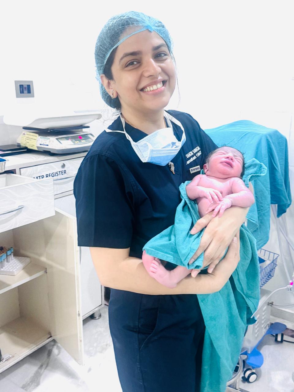 Dr. Shachi Singh smiling while holding a newborn baby in the delivery room after a successful birth